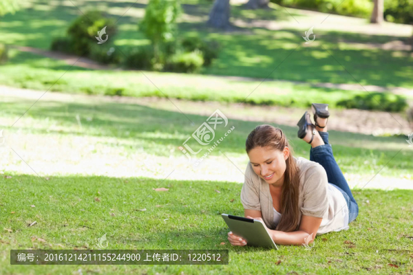 微笑的女子躺在草坪上用平板電腦