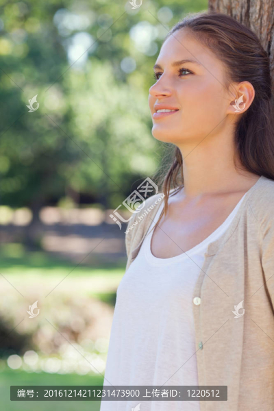 微笑的女人倚著公園里的一棵樹