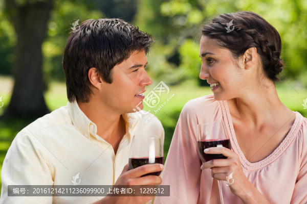 一男一女在公園里互相捧著一杯紅酒互相微笑