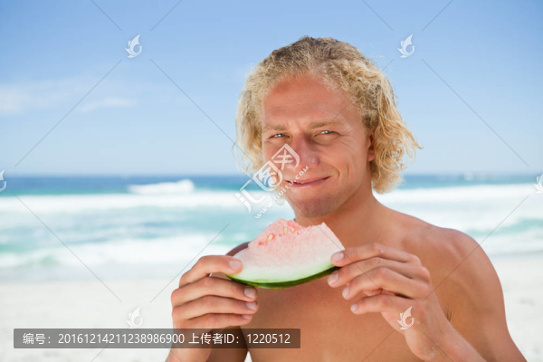 站在海洋前面的人拿著一塊西瓜微笑著