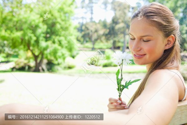 公園長(zhǎng)椅上一個(gè)女人聞到一朵花的側(cè)面