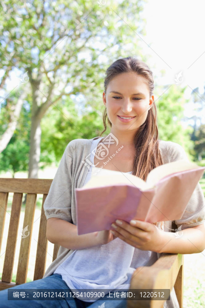 微笑的女人在公園長椅上看書