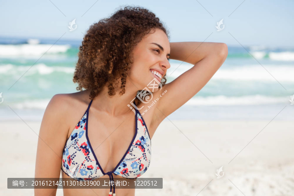 在海灘上穿著泳裝的年輕女子把手放在頭發(fā)上