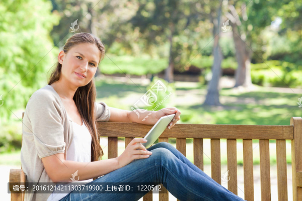 公園長椅上一個帶著平板電腦的女人的側面圖