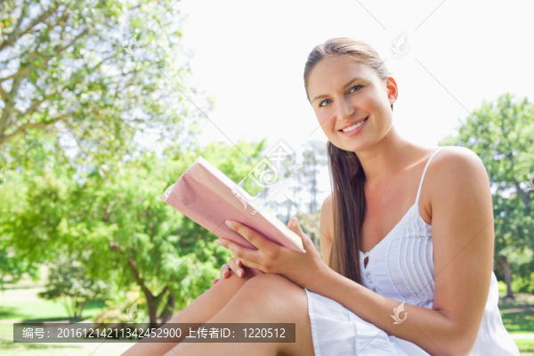 一個面帶微笑的女人在草坪上看書