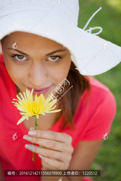 戴著白色帽子的女人一邊看著相機(jī)一邊聞著花