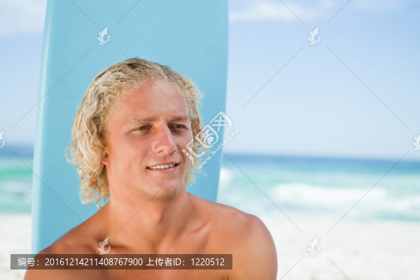微笑的年輕人坐在海灘上與他的沖浪板