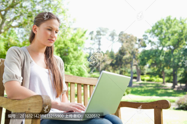 在公園長椅上帶著筆記本電腦的女人