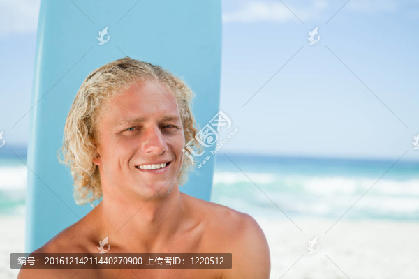 微笑的年輕人坐在前面的海洋和他的沖浪板
