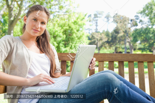 在公園長椅上坐著筆記本電腦的女人