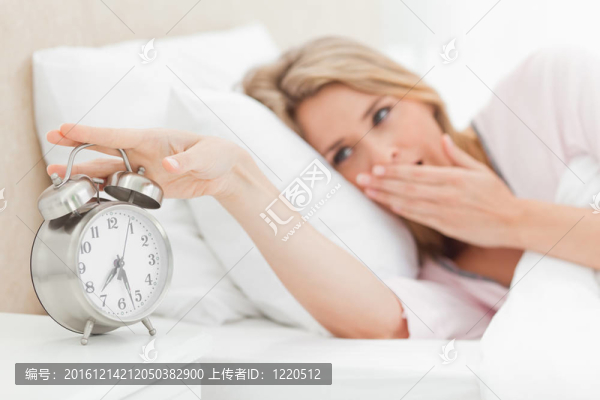 一個(gè)躺在床上的女人打呵欠，伸手去把床邊的鬧鐘響起來。