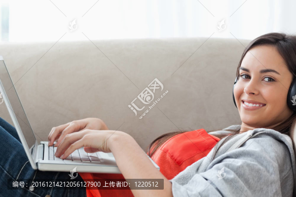 一個靠近一個微笑的年輕女人用她的耳機和筆記本電腦為她看著攝像機鏡頭