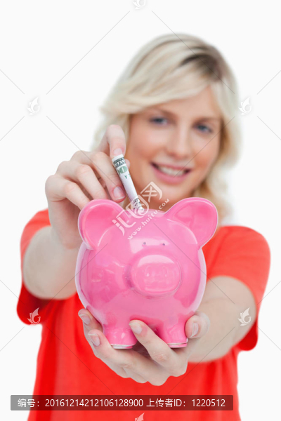 年輕的金發(fā)女人把鈔票放進(jìn)粉紅色的存錢罐