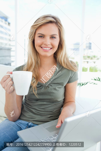 一個女人微笑著，用筆記本電腦，手里拿著一個杯子，一邊看著她。