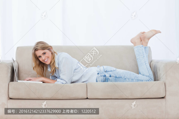 一個(gè)面帶微笑的女人躺在沙發(fā)上用筆記本電腦