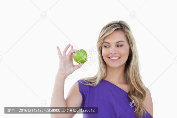 快樂(lè)的年輕金發(fā)女人看著一個(gè)綠色的蘋(píng)果