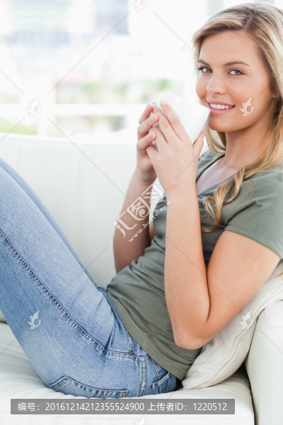 一張?zhí)貙戠R頭，一個(gè)女人側(cè)身坐在沙發(fā)上，手里拿著一只杯子，舉著嘴唇，微笑著向前看。