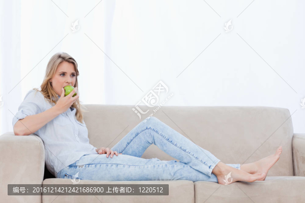 一個(gè)躺在沙發(fā)上的女人正在吃蘋果