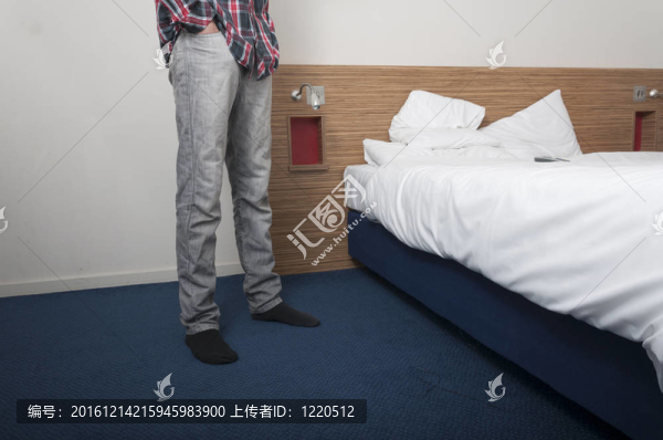 男子站在酒店房間床旁。腰下視圖。