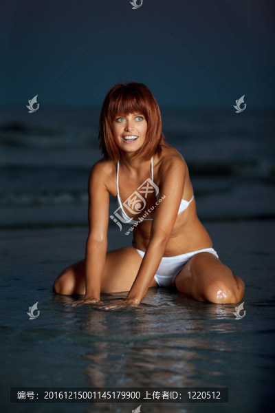 美麗的年輕女子坐在海邊的水；
