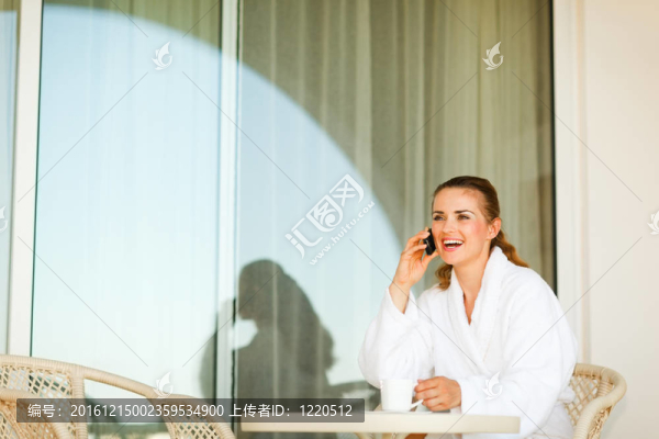 女人笑著在浴袍坐在桌邊喝咖啡和講手機(jī)平臺(tái)