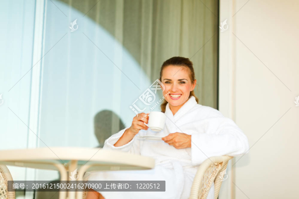在浴袍坐在桌子上露臺(tái)，有杯咖啡有魅力的女人