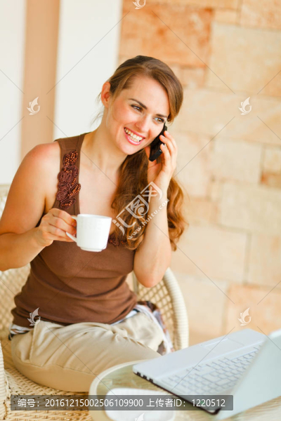 微笑的女人坐在陽臺上，筆記本電腦和一杯茶和說手機
