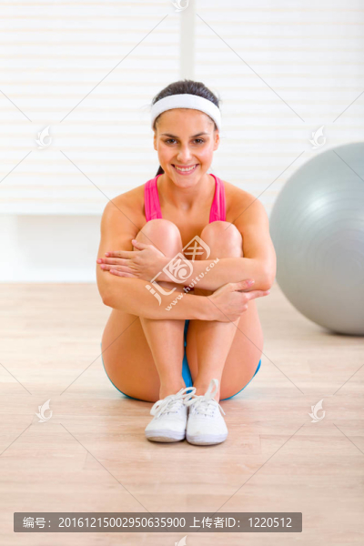 面帶微笑的女孩穿著運動裝坐在家里地板上