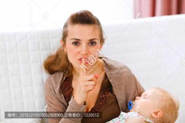 年輕的媽媽抱著熟睡的嬰兒，顯示出噓的手勢