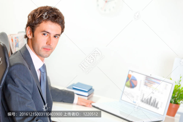 嚴(yán)肅的現(xiàn)代商人坐在辦公桌與筆記本電腦