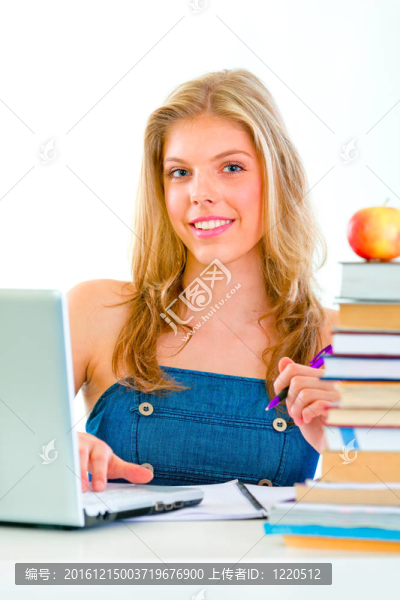 面帶微笑的漂亮女孩坐在桌旁，手里拿著書和筆記本電腦