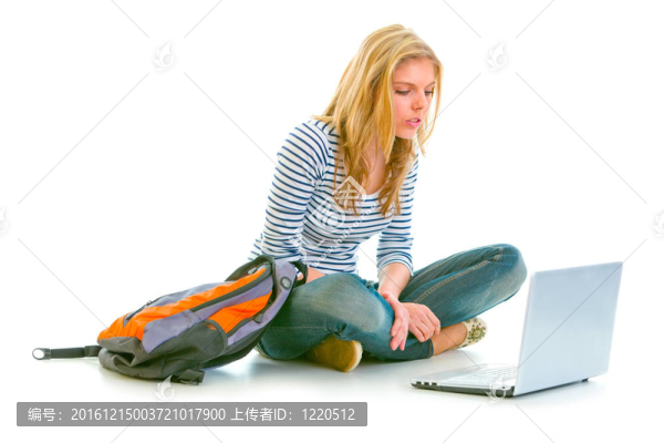有興趣的漂亮女孩坐在地板上背包和看筆記本電腦上孤立的白色