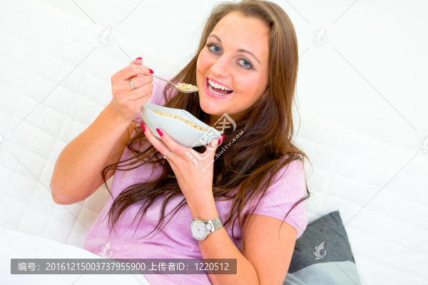 微笑的美麗的女人坐在沙發(fā)上在家里吃早餐