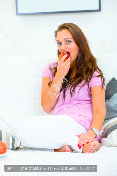 漂亮的女人坐在家里的沙發(fā)上吃蘋(píng)果