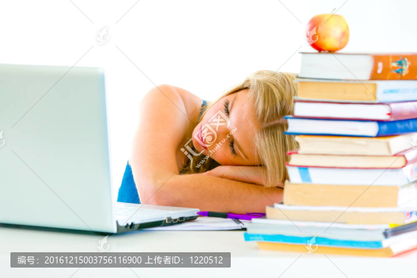 疲憊的年輕女孩在桌子上睡覺，手里拿著書和筆記本電腦