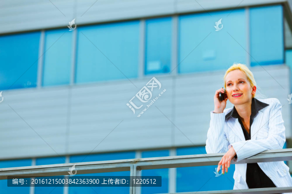 現(xiàn)代商業(yè)女性靠辦公樓欄桿和通話手機