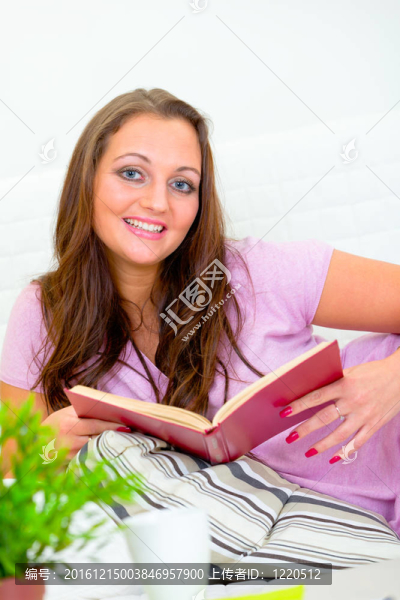 微笑迷人的女人在沙發(fā)上悠閑地在家里看書