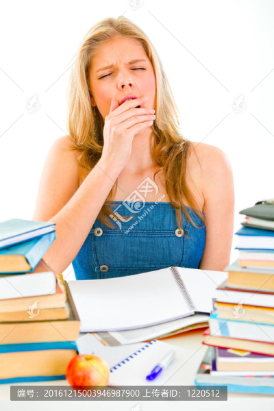 打哈欠的疲倦少女坐在桌上堆著書