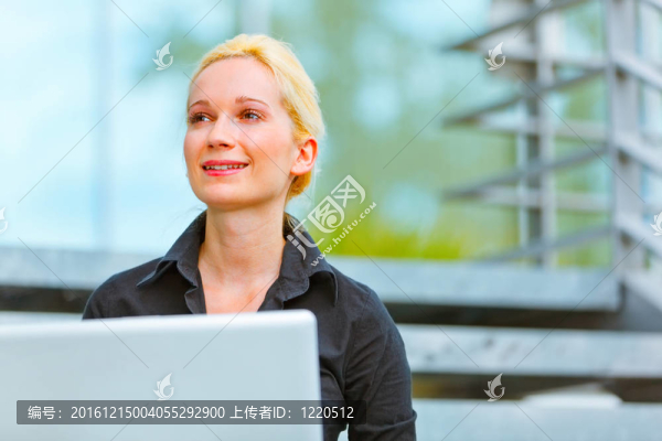 微笑的現(xiàn)代商務(wù)女性坐在辦公樓的樓梯上，使用筆記本電腦