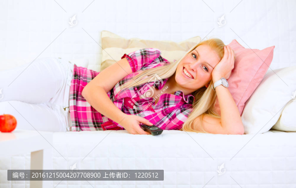 微笑的年輕女子躺在沙發(fā)上看電視