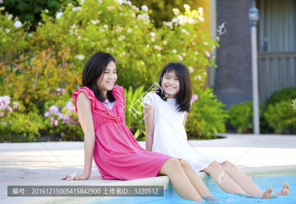兩個年輕女孩坐在游泳池旁；微笑著