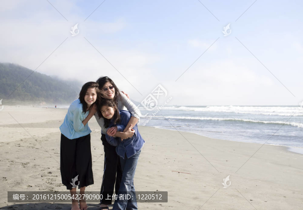 亞洲母親和兩個女兒在海灘上的海洋微笑。