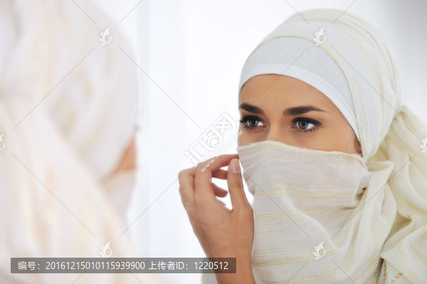 美麗的穆斯林婦女看著鏡子，戴上圍巾