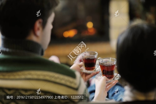 快樂的年輕情侶坐在家里壁爐前的沙發(fā)上