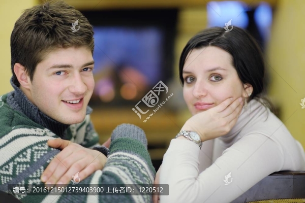 快樂的年輕情侶坐在家里壁爐前的沙發(fā)上