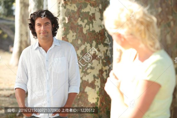 一個男人和一個金發(fā)女人的姿勢藏在樹后面的秘密監(jiān)視他