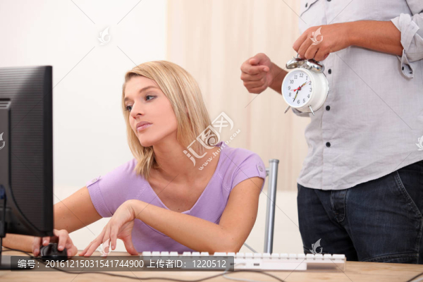 一個(gè)年輕的金發(fā)女人正在做電腦，一個(gè)男人正在發(fā)出鬧鐘