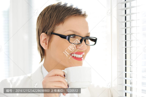 年輕快樂(lè)的商業(yè)女性一邊喝咖啡一邊透過(guò)窗戶(hù)向外看