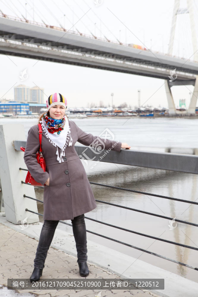 幸福的年輕白人婦女與紅色袋站在堤防。全長。橋的背景