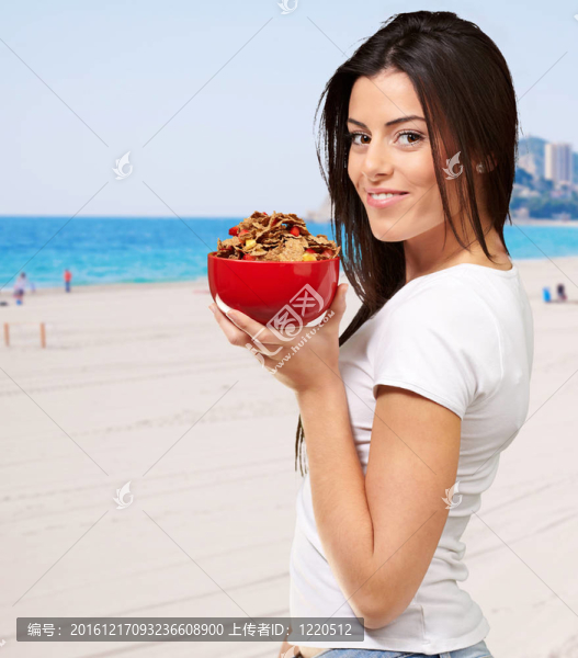 健康的女人拿著碗玉米片在Beach